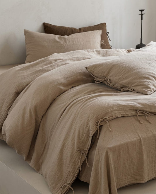 Natural Oat muslin cotton duvet cover and flat sheet with bow tie closures, styled with a brown accent pillow in a minimalist bedroom