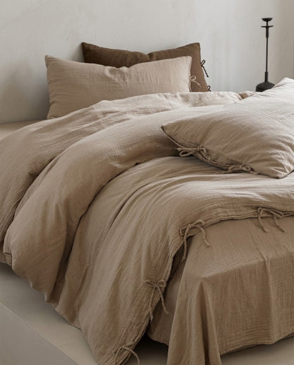 Natural Oat muslin cotton duvet cover and flat sheet with bow tie closures, styled with a brown accent pillow in a minimalist bedroom