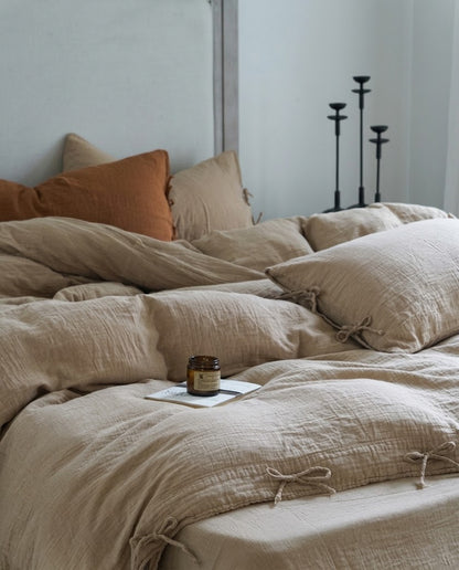 Natural Oat muslin cotton duvet cover set with tie closures, a rust accent pillow, and black candlesticks on a relaxed unmade bed