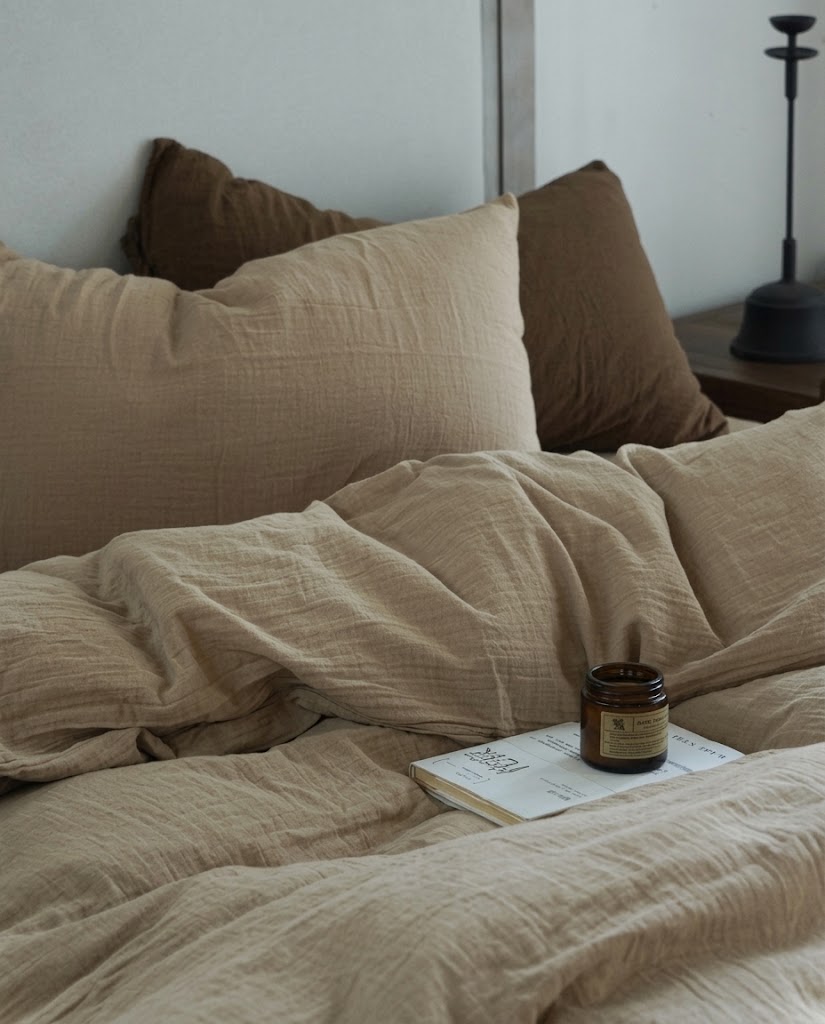 Natural Oat crinkled muslin duvet cover and pillowcases with an amber candle and book in soft natural light
