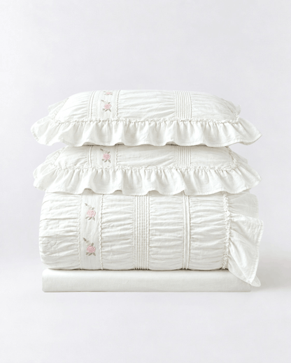 Ivory ruched cotton duvet cover set with pintuck ruffles and embroidered pink roses, folded with two matching pillow shams