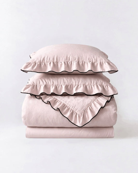 Camellia Ruffled Duvet Cover Set in Quartz, folded pale pink duvet cover, flat sheet and ruffled shams with black piping