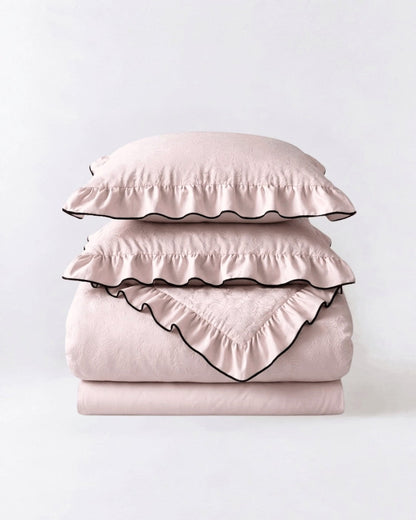 Camellia Ruffled Duvet Cover Set in Quartz, folded pale pink duvet cover, flat sheet and ruffled shams with black piping
