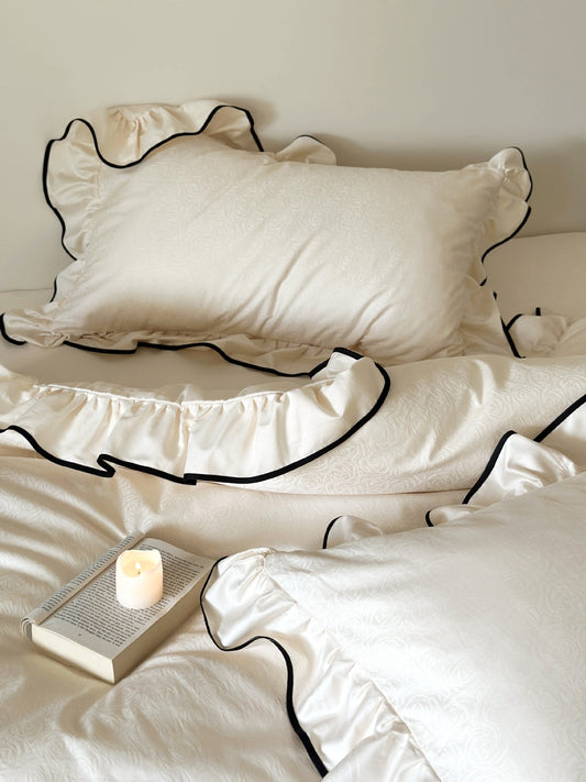 Camellia Ruffled Duvet Cover Set in Ivory with rose jacquard pillow shams, styled with a candle and book