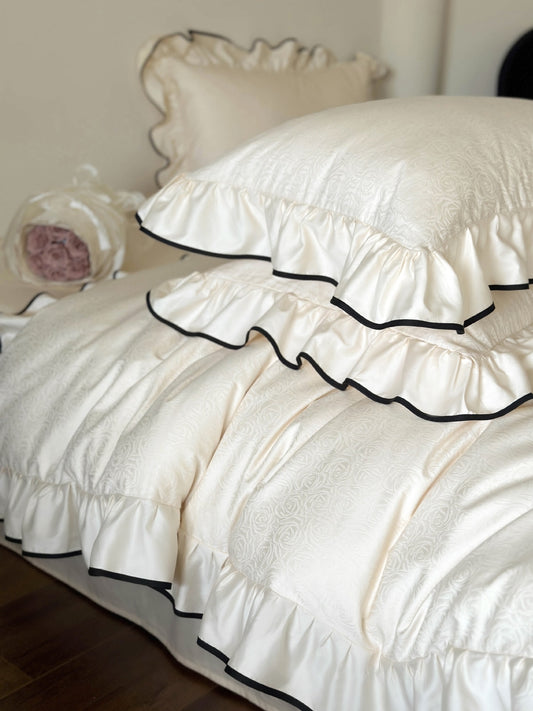 Close-up of ruffled edges with black piping on the Camellia Ruffled Duvet Cover Set in Ivory