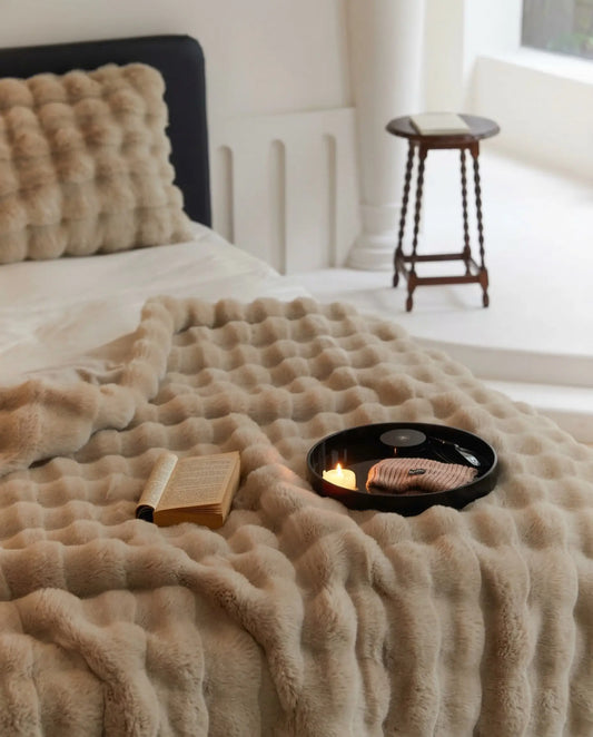 DORMÉ Studio Marshmallow Ultra Plush Blanket in khaki plush fabric styled on bed with book and candle creating cozy bedroom aesthetic. Khaki