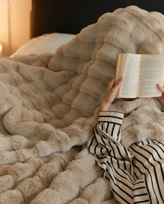 Person reading book in bed wrapped in DORMÉ Studio Marshmallow Ultra Plush Blanket khaki plush texture. Khaki