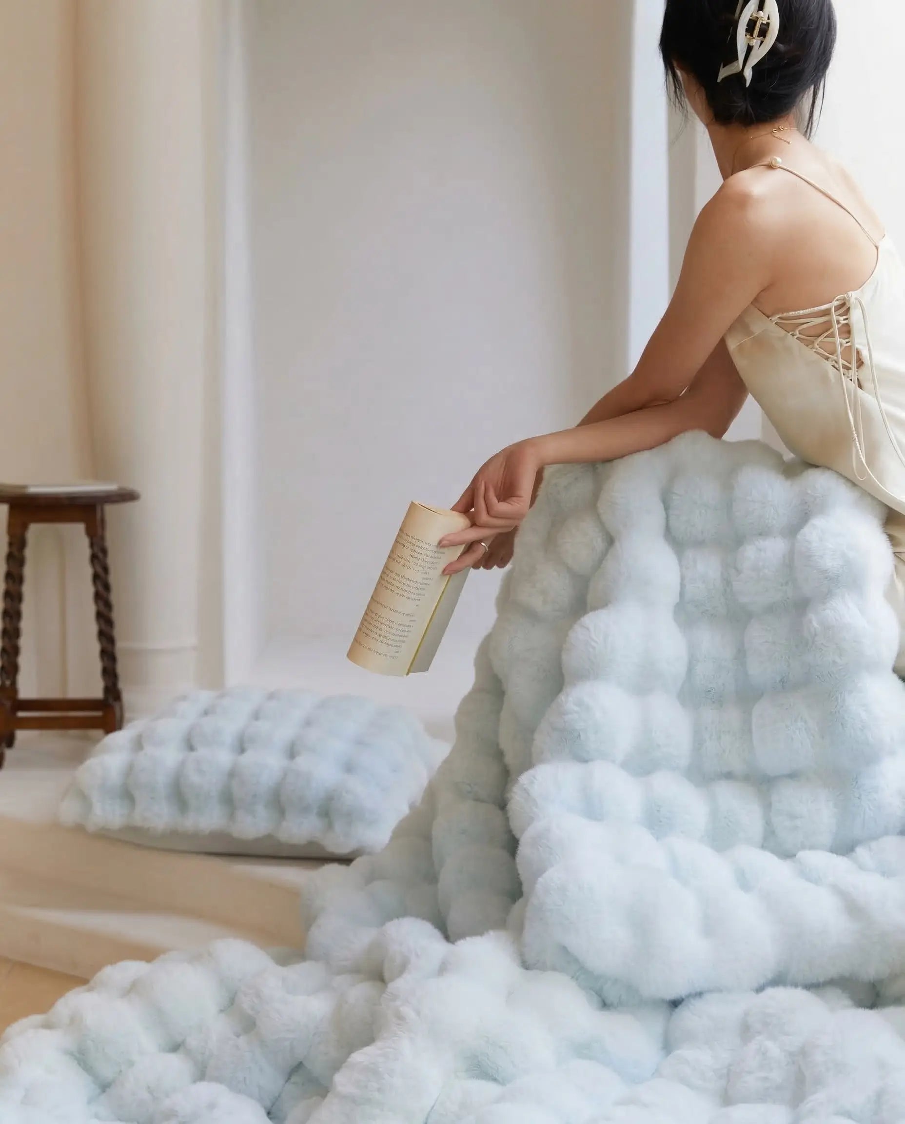 DORMÉ Studio Marshmallow Ultra Plush Blanket draped over bed while woman relaxes holding a book highlighting plush sculpted texture.