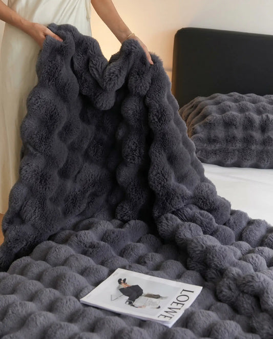 Person lifting DORMÉ Studio Marshmallow Ultra Plush Blanket in charcoal plush fabric showing thick sculpted texture. Black