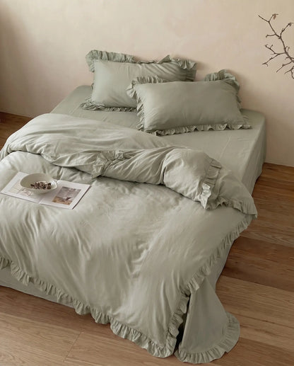 Luxury eucalyptus sage duvet cover set with matching ruffle pillow shams styled on a minimalist bed by DORMÉ Studio