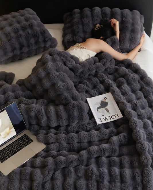 Woman resting in bed under DORMÉ Studio Marshmallow Ultra Plush Blanket charcoal plush texture with laptop and magazine. Black