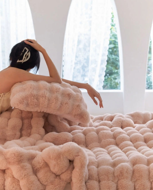 Woman resting on DORMÉ Studio Marshmallow Ultra Plush Blanket in pink plush texture creating a cozy luxury bedroom aesthetic. Blossom