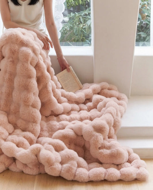 DORMÉ Studio Marshmallow Ultra Plush Blanket pink plush texture cascading across floor near window. Blossom