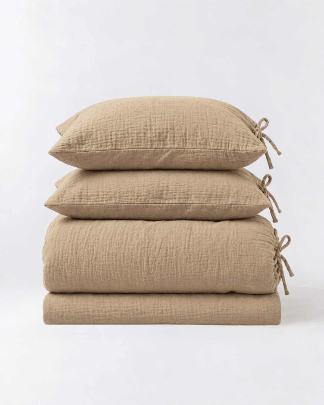 Folded Natural Oat muslin cotton duvet cover set by DORMÉ Studio showing duvet cover, flat sheet, and two tie-closure pillowcases