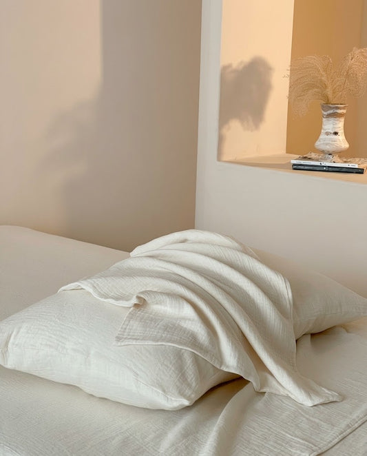 Pearl muslin cotton double gauze duvet cover draped over a matching pillowcase beside a dried grass vase