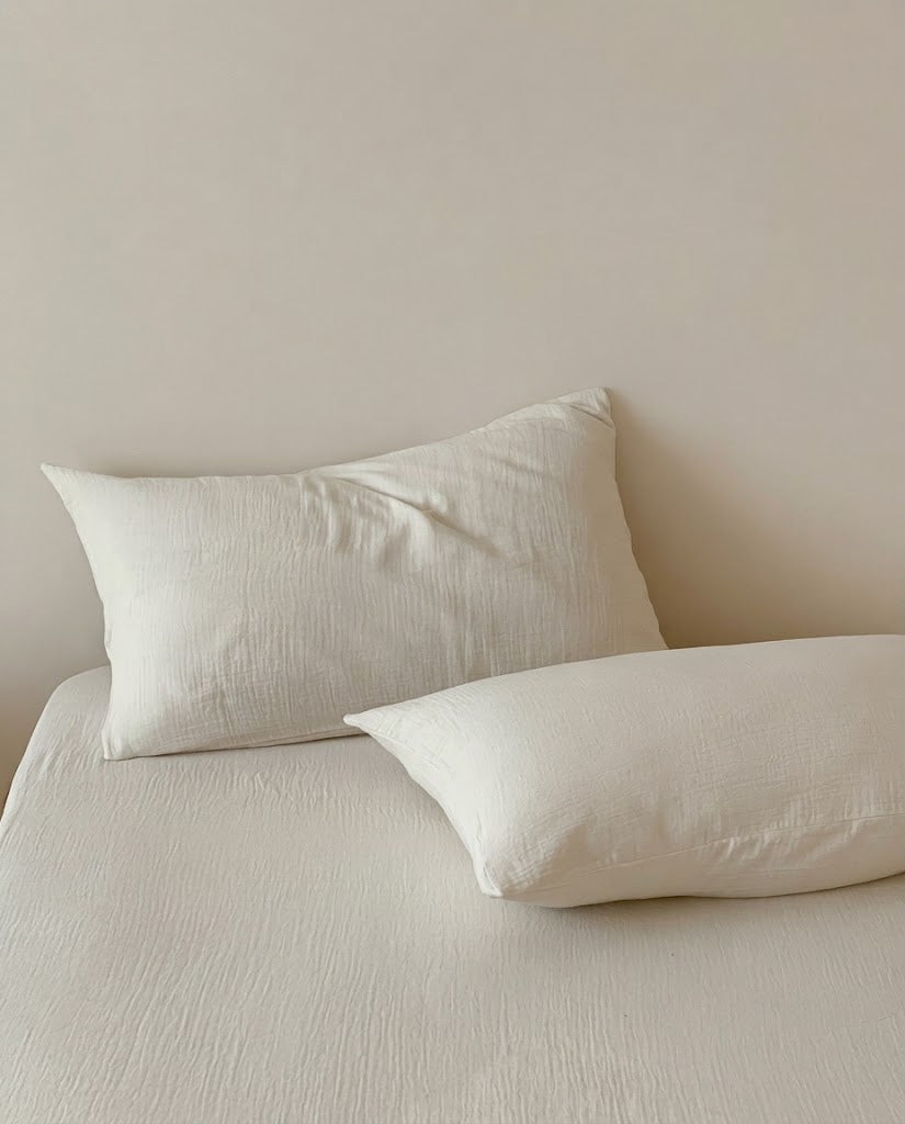 Two Pearl muslin cotton double gauze pillowcases on a matching sheet against a cream wall