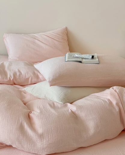 Petal muslin cotton double gauze pillowcases on a softly rumpled duvet cover with an open book