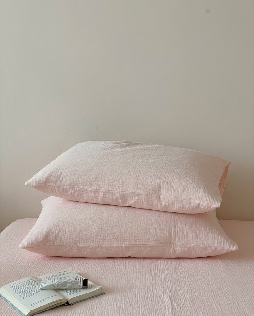 Two Petal muslin cotton double gauze pillowcases stacked on a matching sheet with an open book