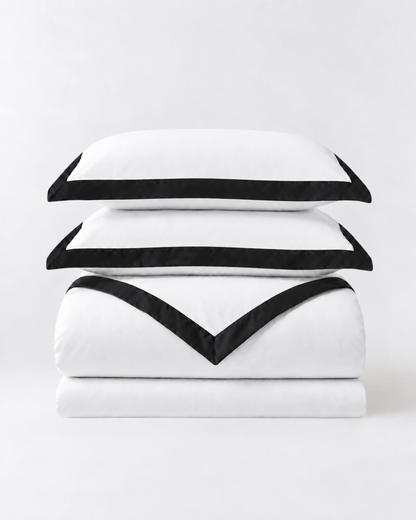 Folded white duvet cover set with black trim and matching pillowcases on neutral studio background