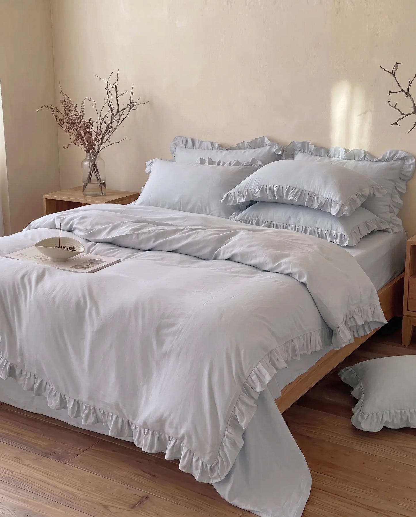 Bed with light blue gray ruffled bedding in a bedroom setting.