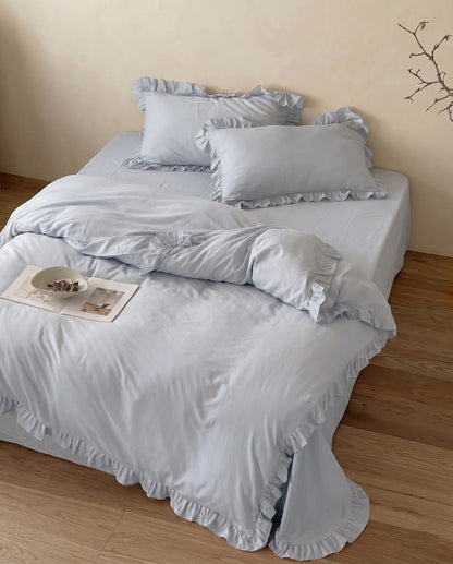 Mist blue luxury bedding set with soft ruffle details styled in an airy neutral bedroom by DORMÉ Studio