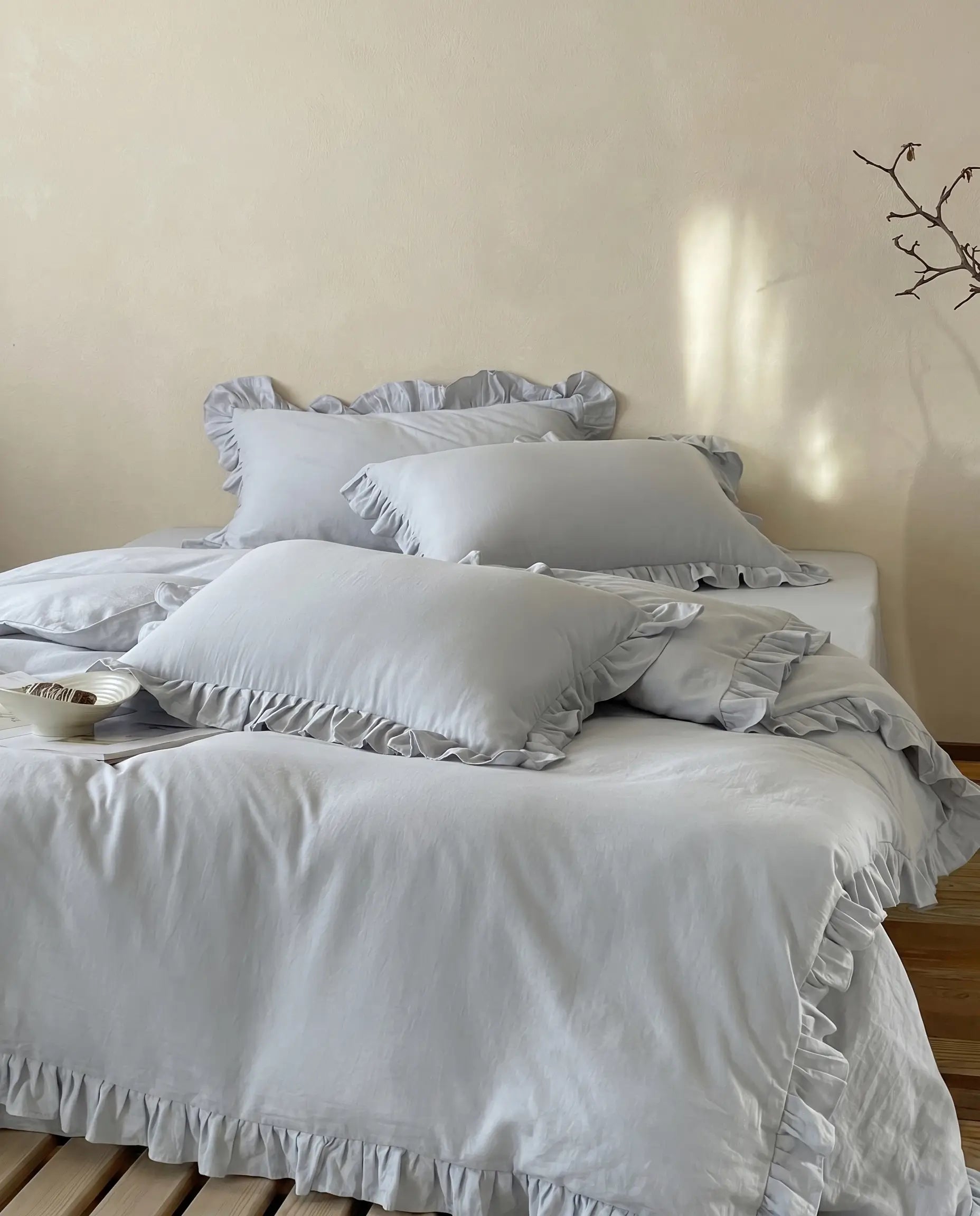Mist blue ruffle duvet cover set styled in a warm neutral bedroom with soft luxury bedding and elegant layered pillows