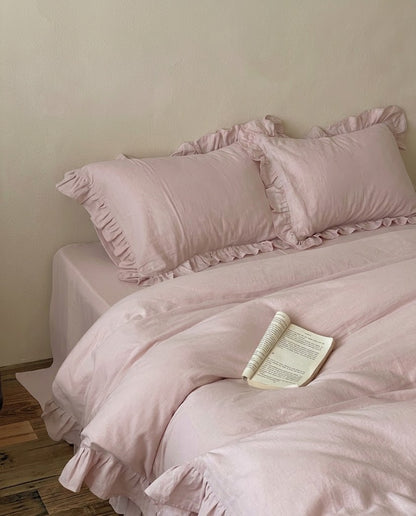 Rosalie blush pink ruffle duvet cover set in soft 100% cotton on a made bed with matching ruffle pillow shams and an open book