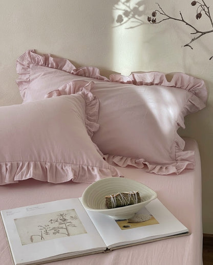 Blush pink ruffle pillow shams from the Rosalie duvet cover set by DORMÉ Studio, styled in a sunlit bedroom with an open art book