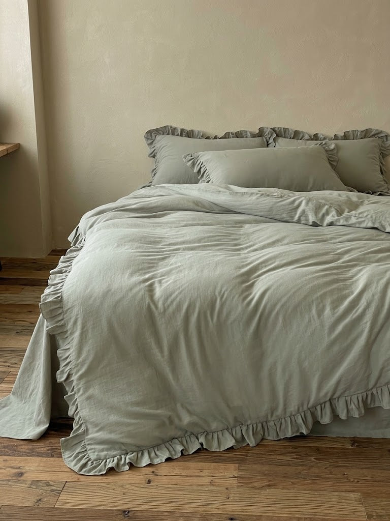 Rosalie eucalyptus sage ruffle duvet cover set in 100% cotton on a full bed with layered pillow shams and a ruffle hem over a wood floor