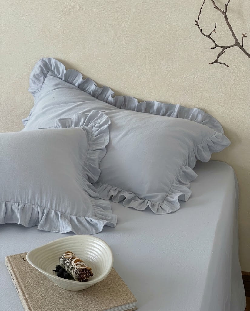 Layered mist blue ruffle pillow shams from the Rosalie duvet cover set in 100% cotton, styled with a ceramic bowl and linen bound book