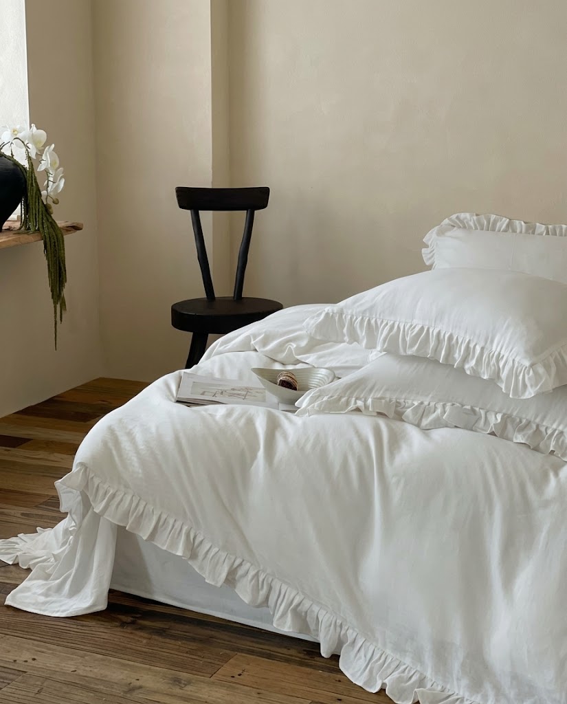 Snow white ruffle duvet cover set on a bed in a minimalist bedroom with a black wooden chair, orchid and ruffle hem on wood floor