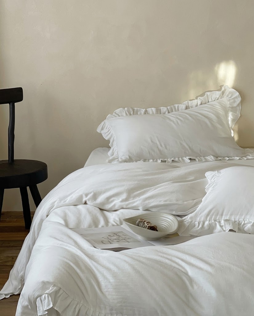 Snow white Rosalie ruffle duvet cover set in soft cotton on a bed with sunlit ruffle pillow shams and a black wooden stool