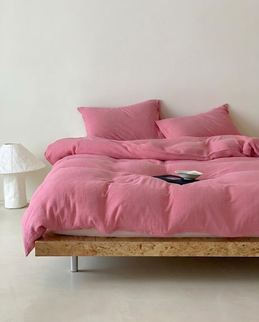 Rose muslin cotton double gauze duvet cover and pillowcases on a wooden platform bed beside a white lamp