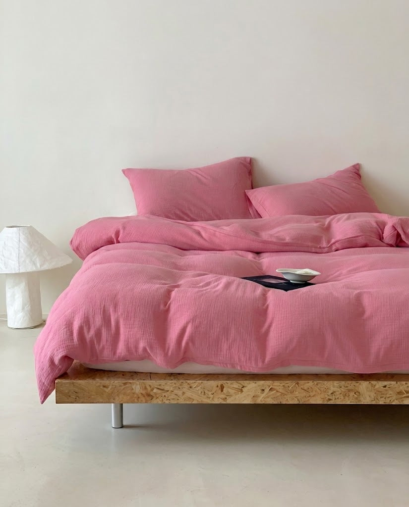 Rose muslin cotton double gauze duvet cover and pillowcases on a wooden platform bed beside a white lamp