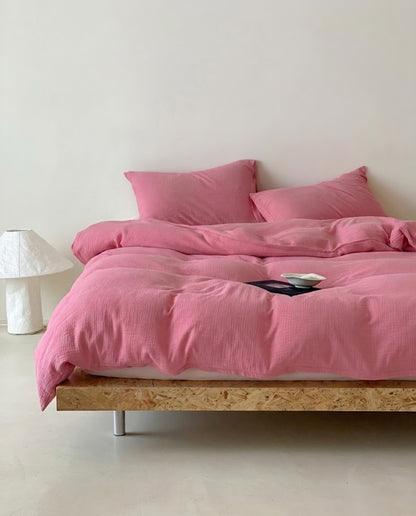 Rose muslin cotton double gauze duvet cover and pillowcases on a wooden platform bed beside a white lamp