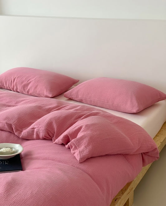 Rose muslin cotton double gauze duvet cover and pillowcases on an unmade bed with a white fitted sheet