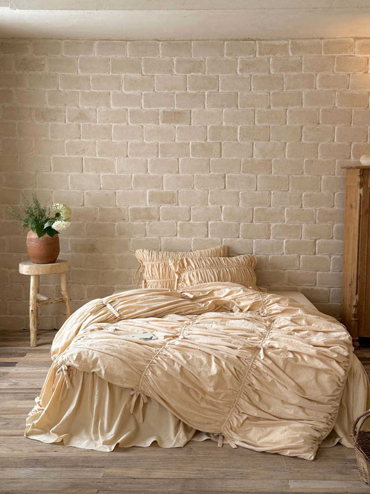 Front view of a cream ruched duvet cover set with bow ties, ruched pillowcases and ruffled bed skirt in washed cotton