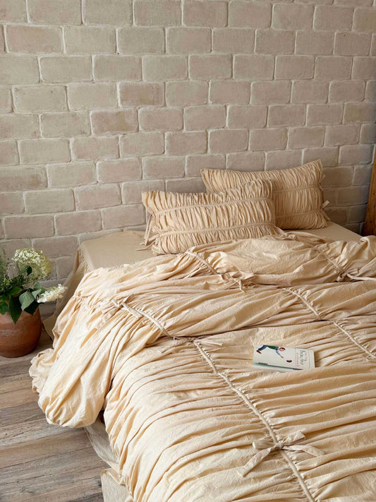 Cream ruched duvet cover with bow ties and matching ruched pillowcases in 100% washed cotton on a bed against a brick wall