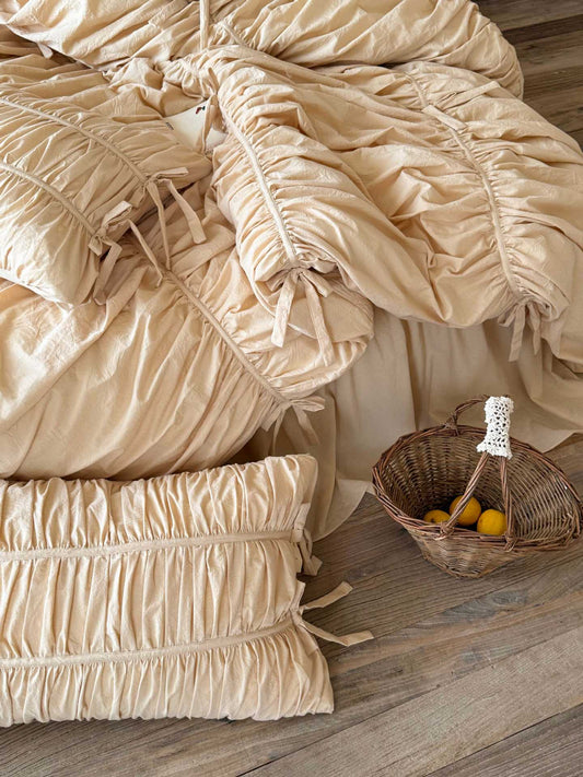 Top-down view of cream washed cotton ruched pillowcase and bow-tied duvet cover with ruffled bed skirt on a wooden floor