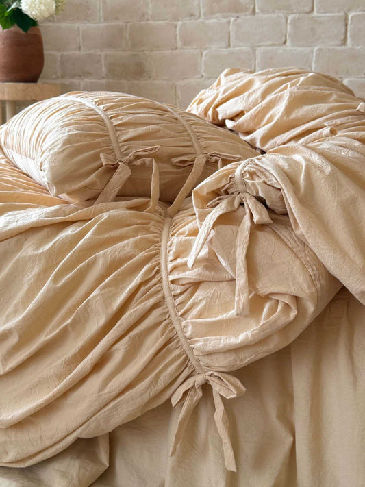Close-up of cotton bow ties on a ruched duvet cover channel and gathered pillowcase in cream washed cotton