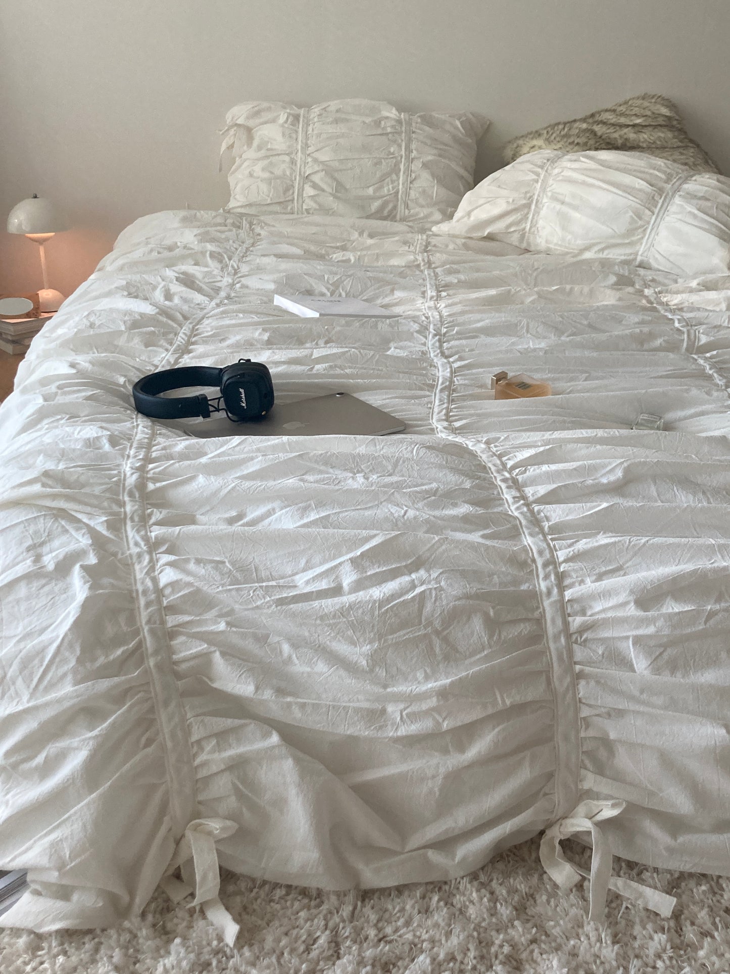 Close-up of white ruched bedding showing gathered cotton fabric detail with Marshall headphones and a MacBook