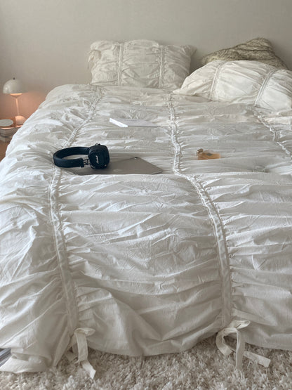 Close-up of white ruched bedding showing gathered cotton fabric detail with Marshall headphones and a MacBook