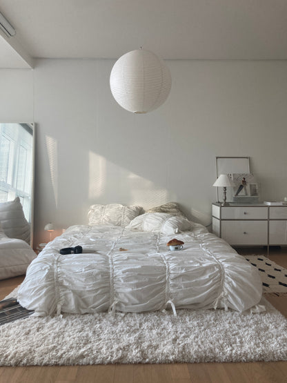 Classic white ruched bedding set in a bright all-white minimalist bedroom with a round paper pendant light and mirrored nightstand