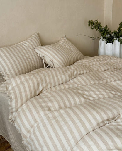 Sable Stripe Duvet Cover Set in oatmeal and cream on a made bed with matching tie pillowcases and pinstripe sheet