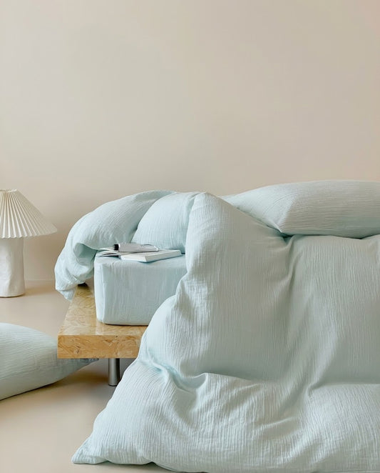 Seafoam muslin cotton double gauze duvet cover draped to the floor with a pillow and pleated lamp