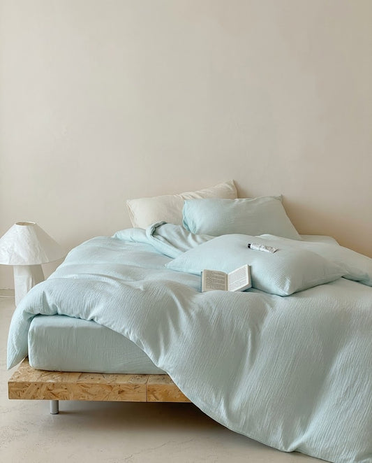 Seafoam muslin cotton double gauze duvet cover set draped over a wooden platform bed beside a paper lamp