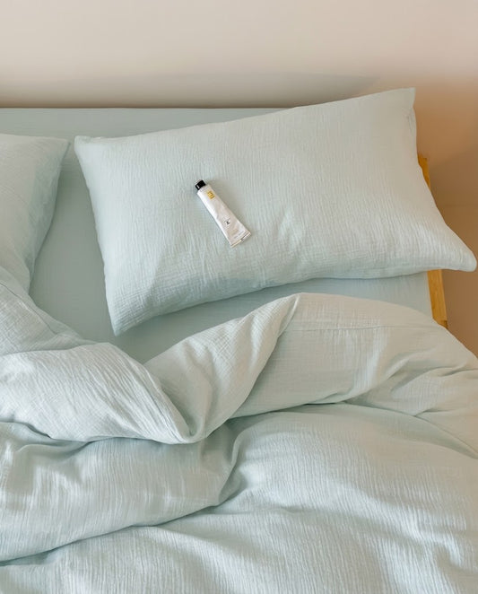 Overhead view of a Seafoam muslin cotton double gauze pillowcase above a softly rumpled duvet cover