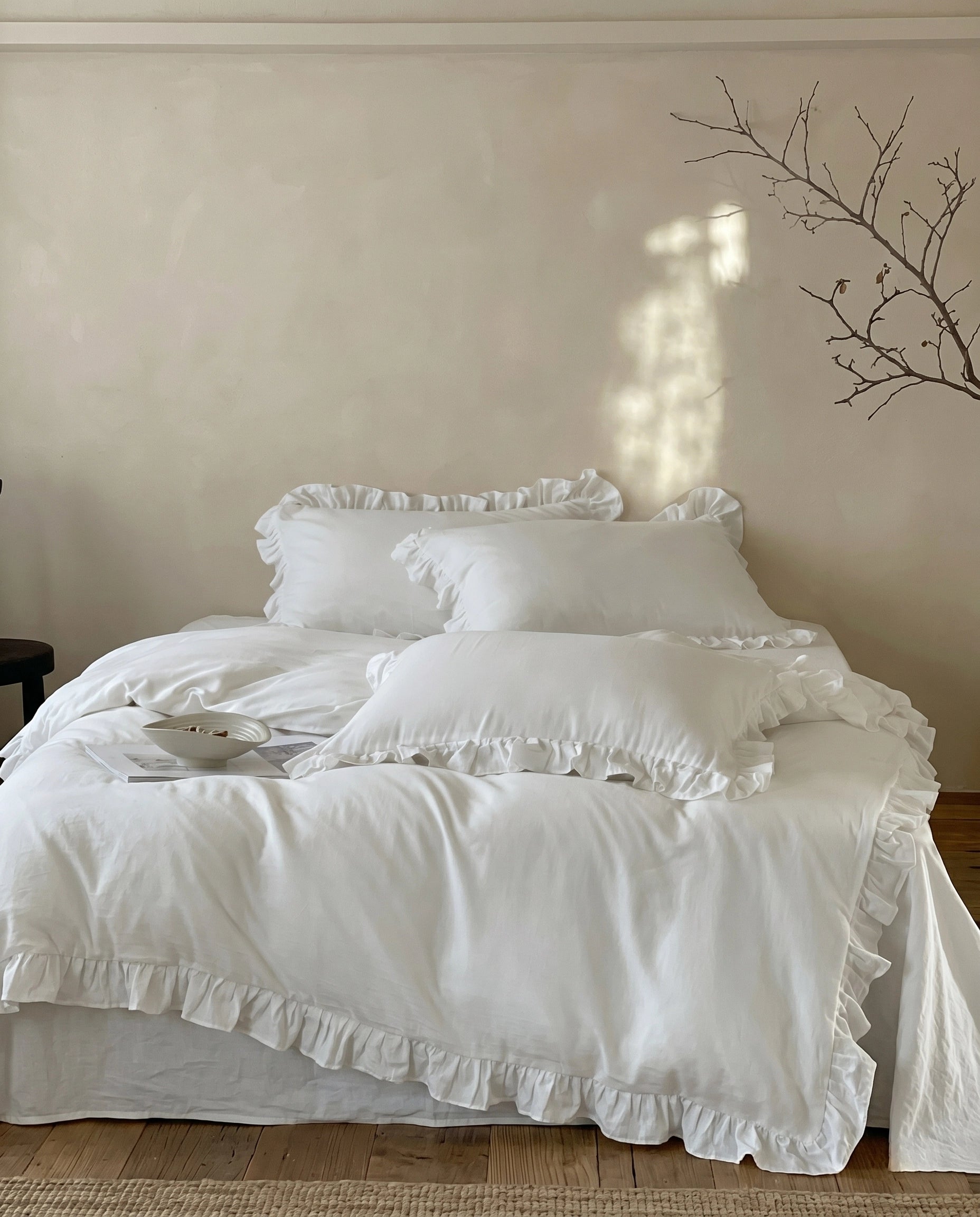 Romantic snow white ruffle bedding set with layered pillows and soft luxury duvet styling in a serene neutral bedroom