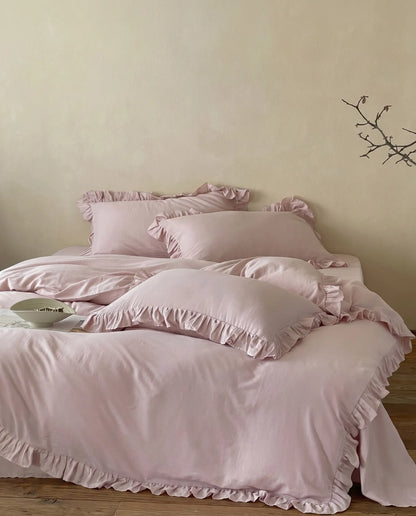 Soft blush pink ruffle bedding styled with layered pillows and elegant feminine bedroom decor aesthetic by DORMÉ Studio