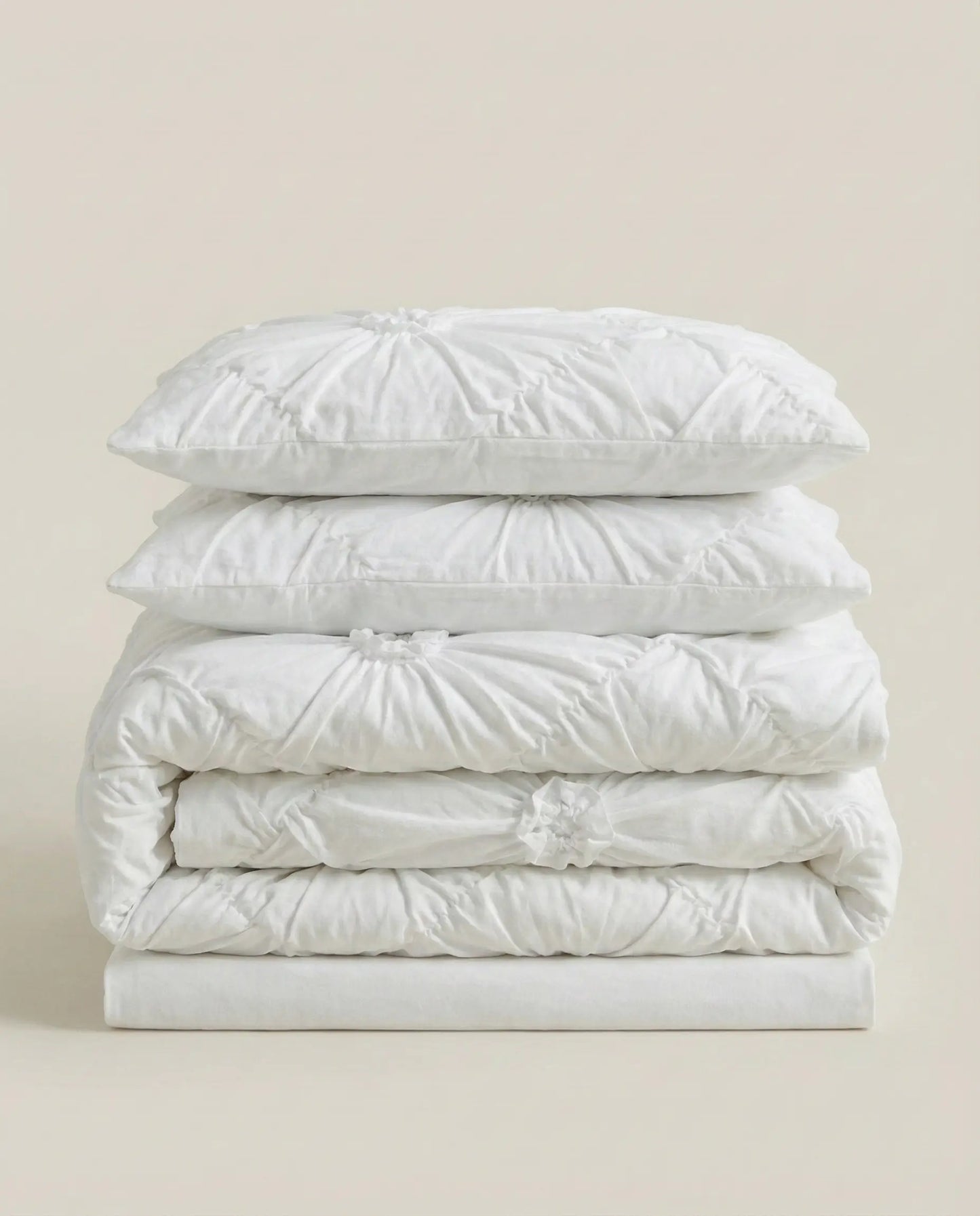 Folded white ruched duvet cover set with matching pillowcases stacked on neutral studio background